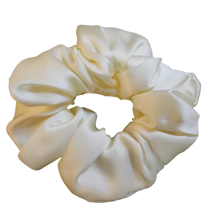 A beige silk scrunchie displayed on a reflective surface.